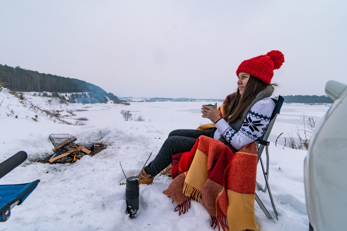 Femme assise sur une chaise de camping dans la neige devant un feu
